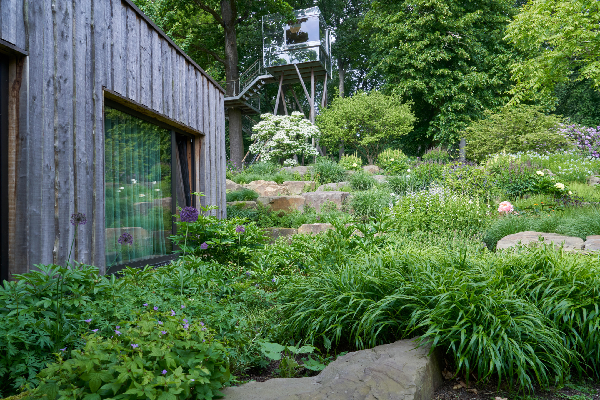 A sloping garden with stones beside a wooden house with a viewpoint in the background