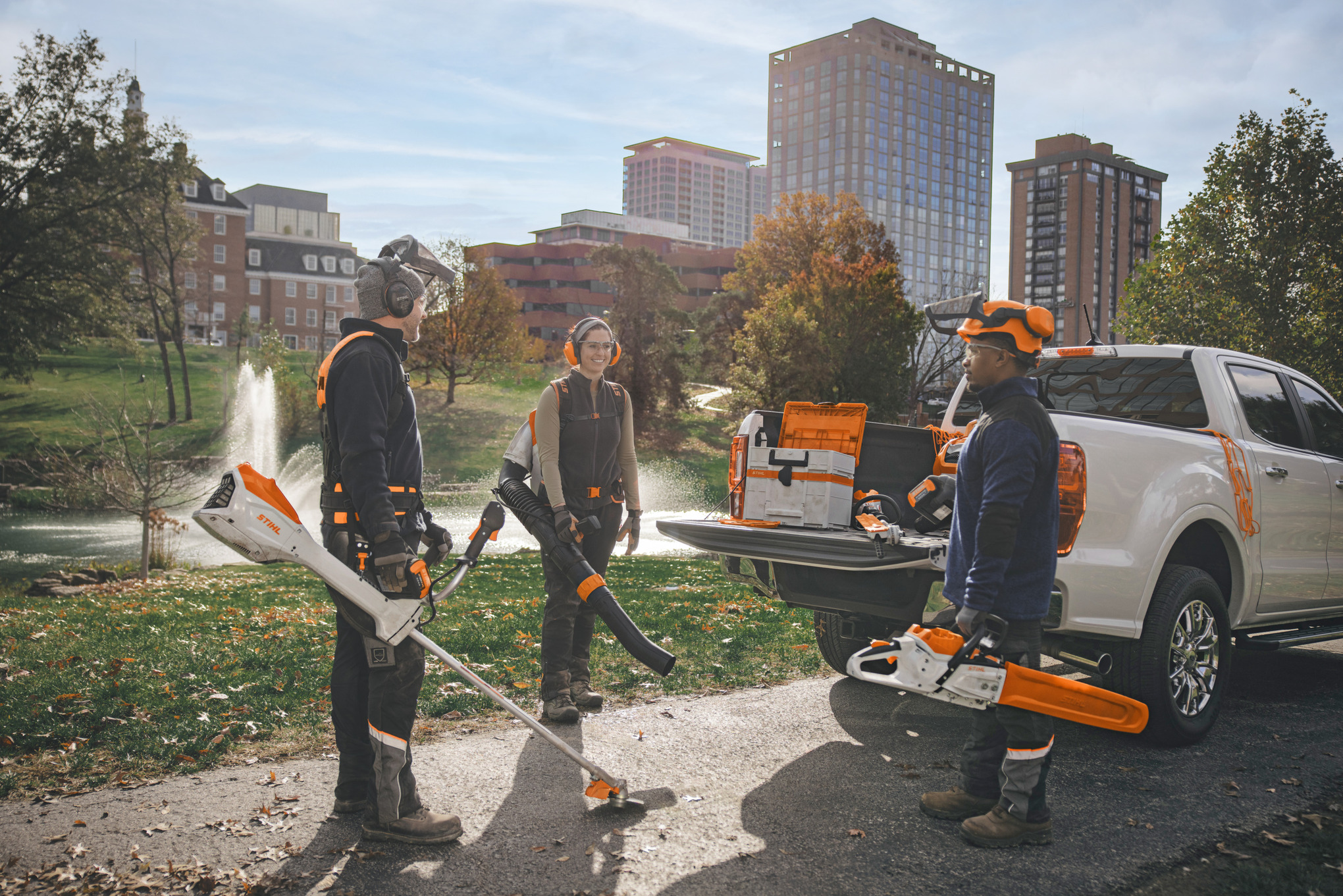 A group of professional landscape gardeners standing around their vehicles preparing themselves to work with STIHL battery power tools. 