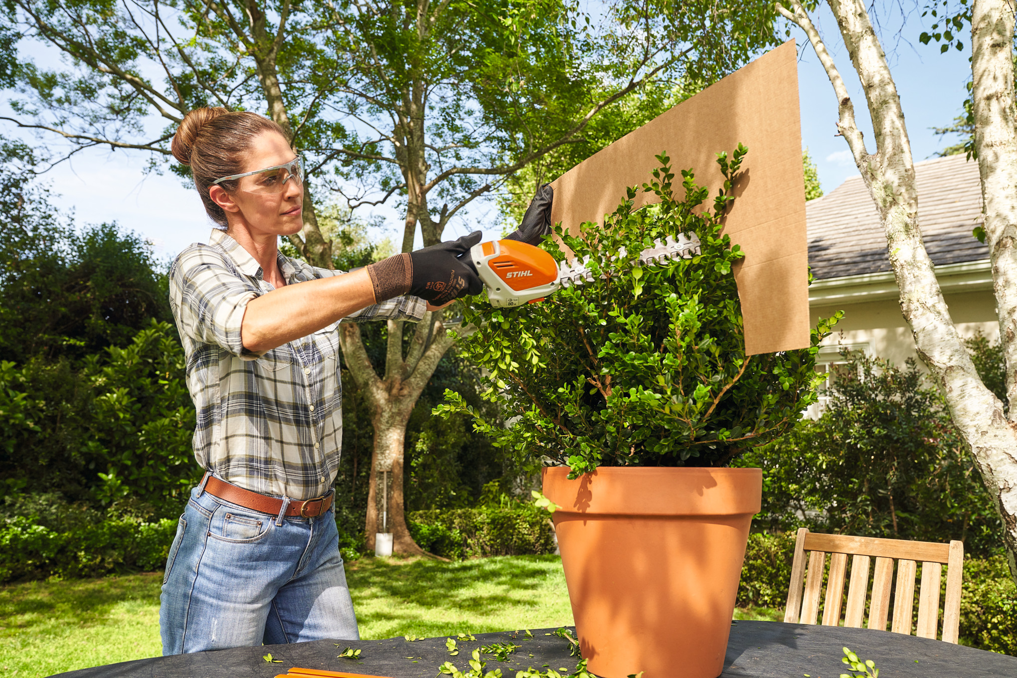 A woman trimming a box bush using STIHL HSA 26 battery shrub shears and a ball-shaped cardboard template