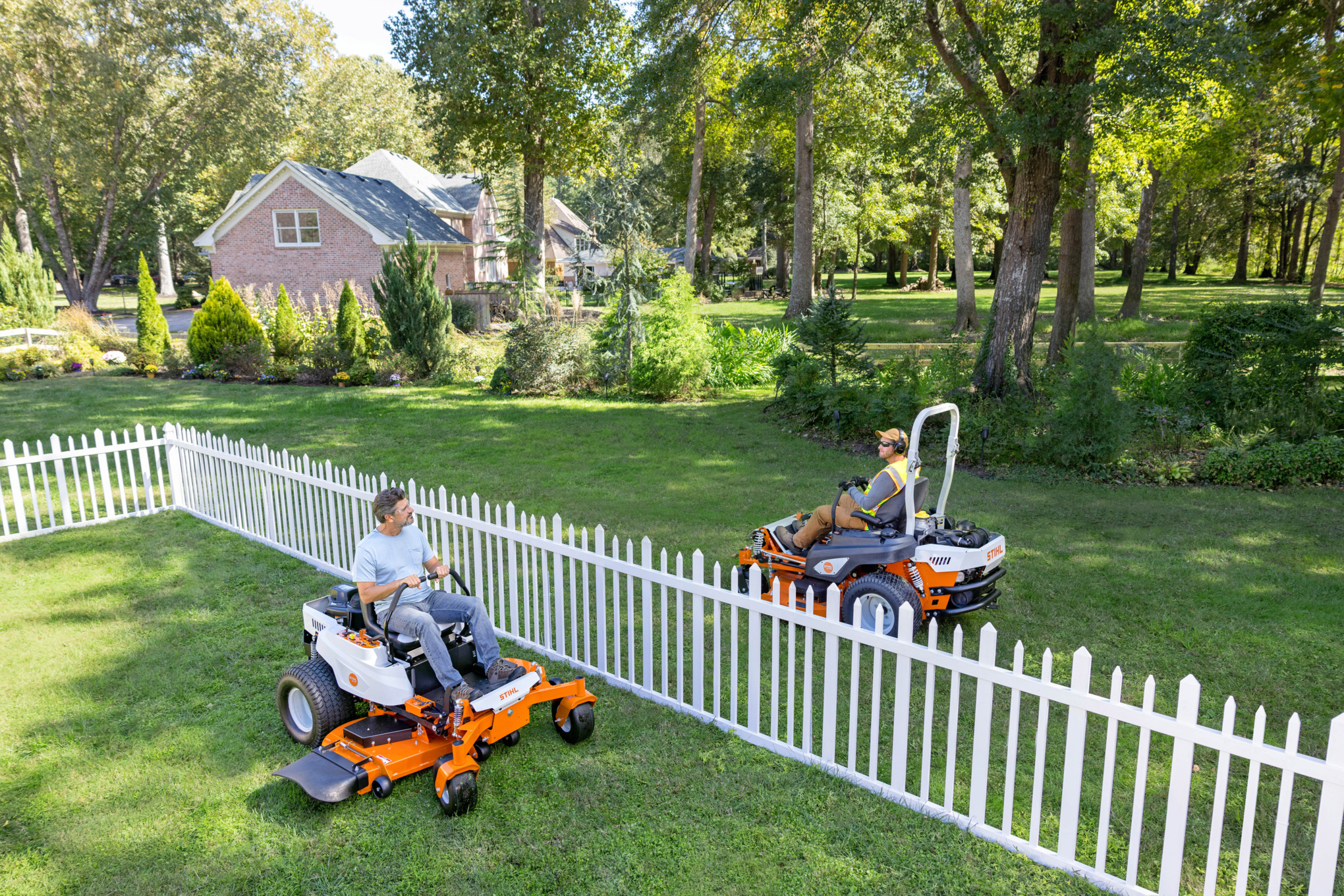 Homeowner and professional landscaper sitting on STIHL Zero-Turns talking across the backyard fence