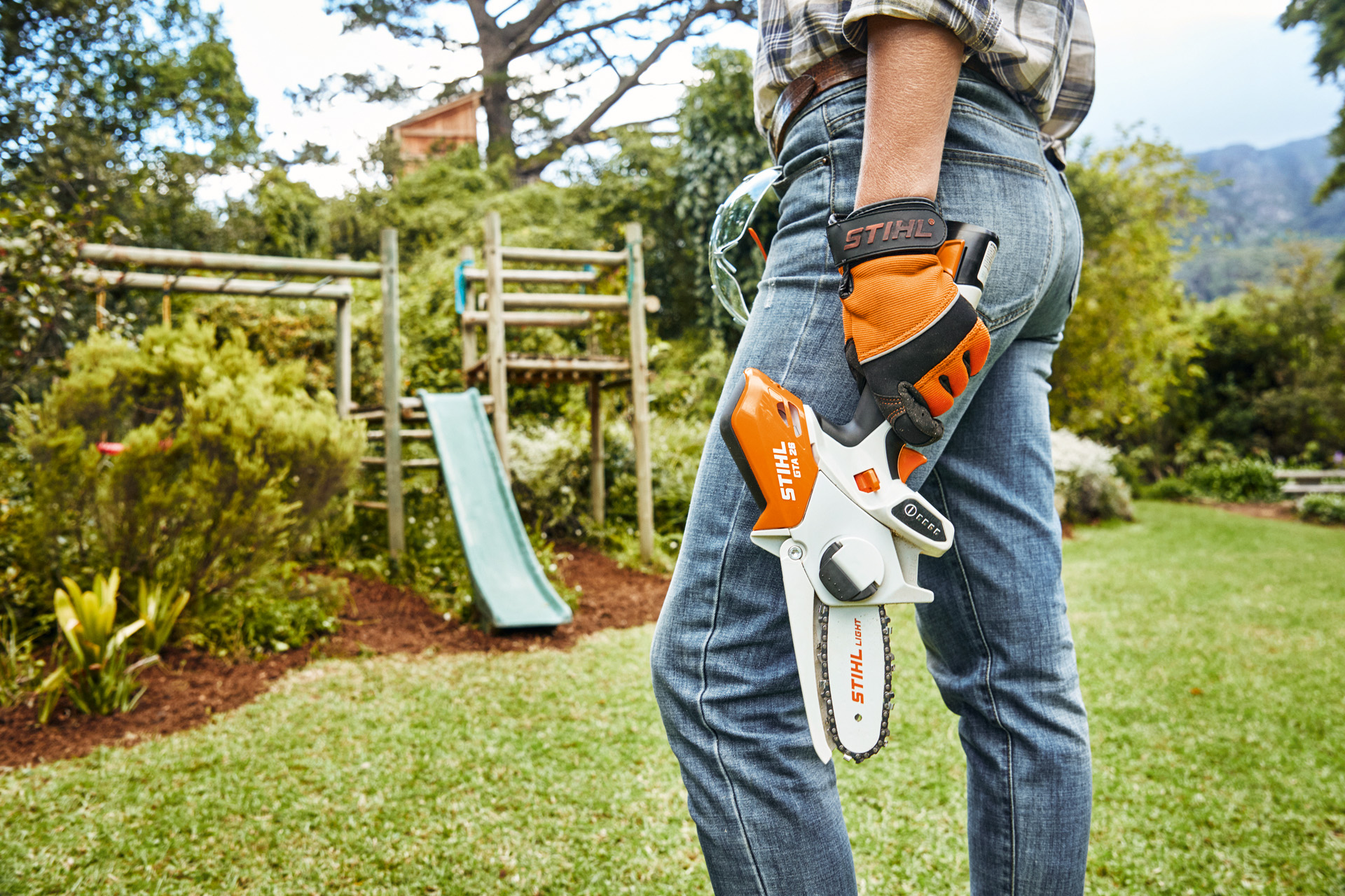 A person with a STIHL GTA 26 battery-powered garden pruner standing in front of a slide in a garden