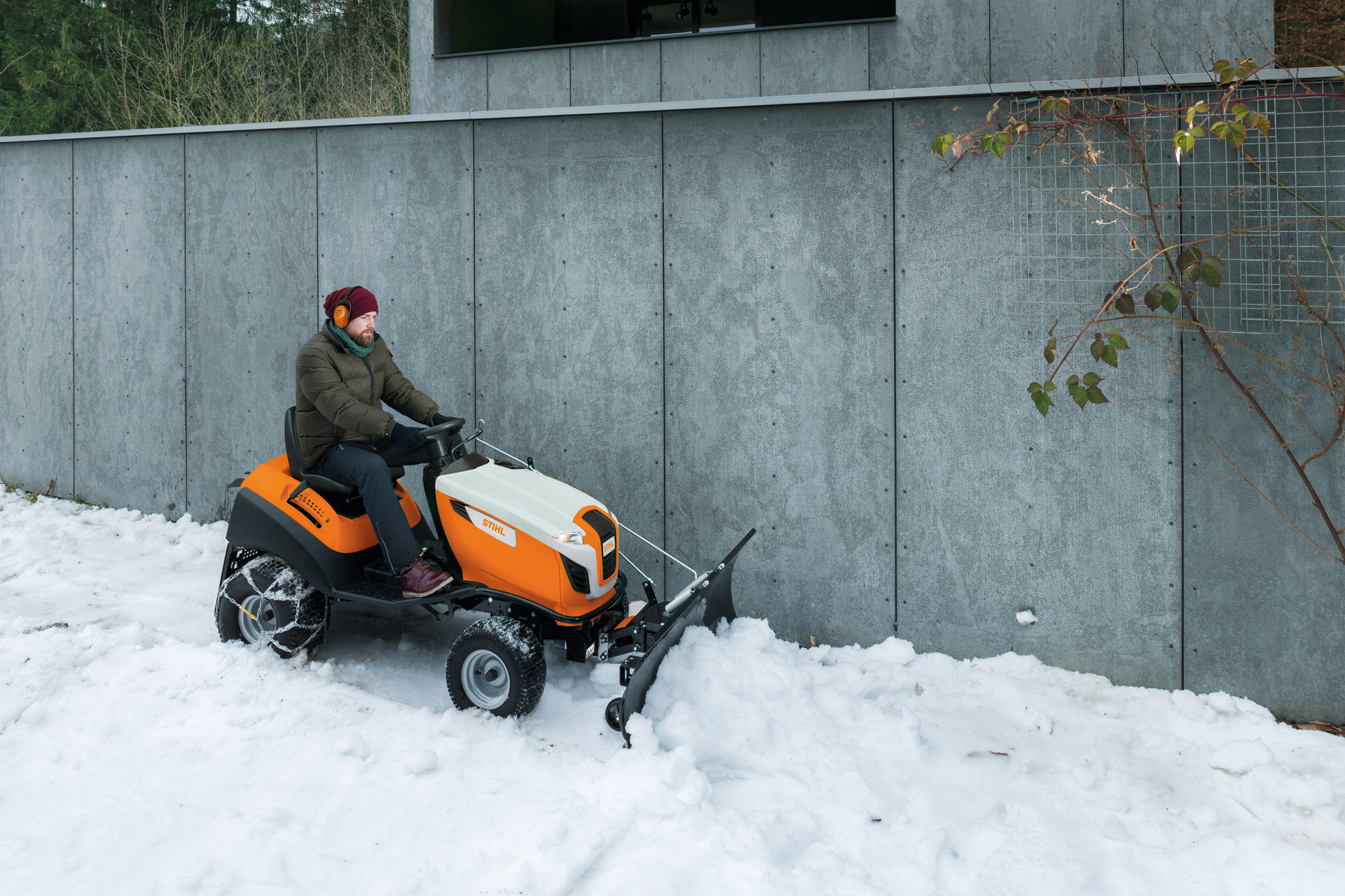 Man clears snow in front of a wall on a snow plough ride-on mower