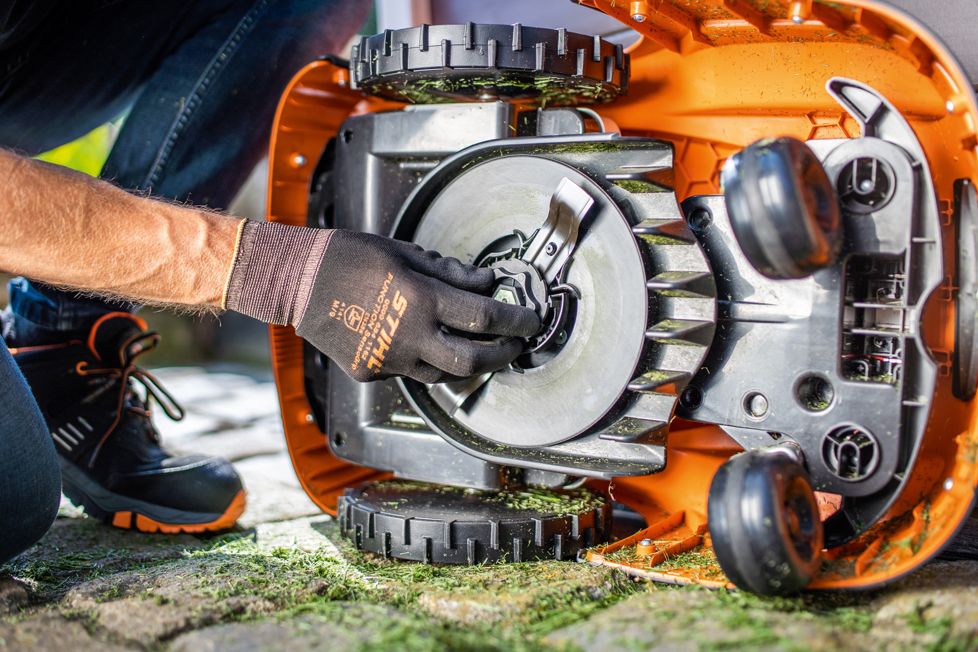 A view of the clean underside of a STIHL iMOW® robot mower, as someone wearing gloves checks the blade