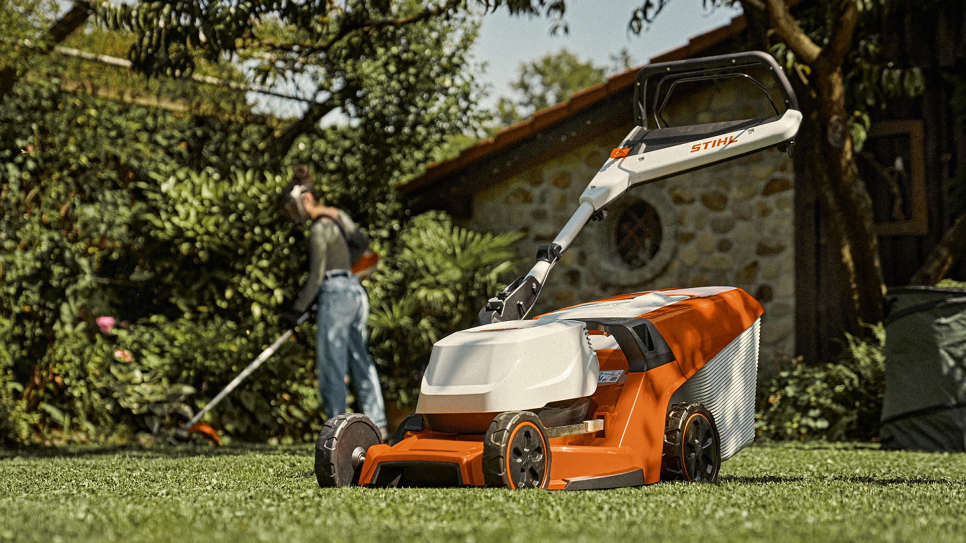 Homeowner trimming a lawn beside a STIHL battery-powered push mower.