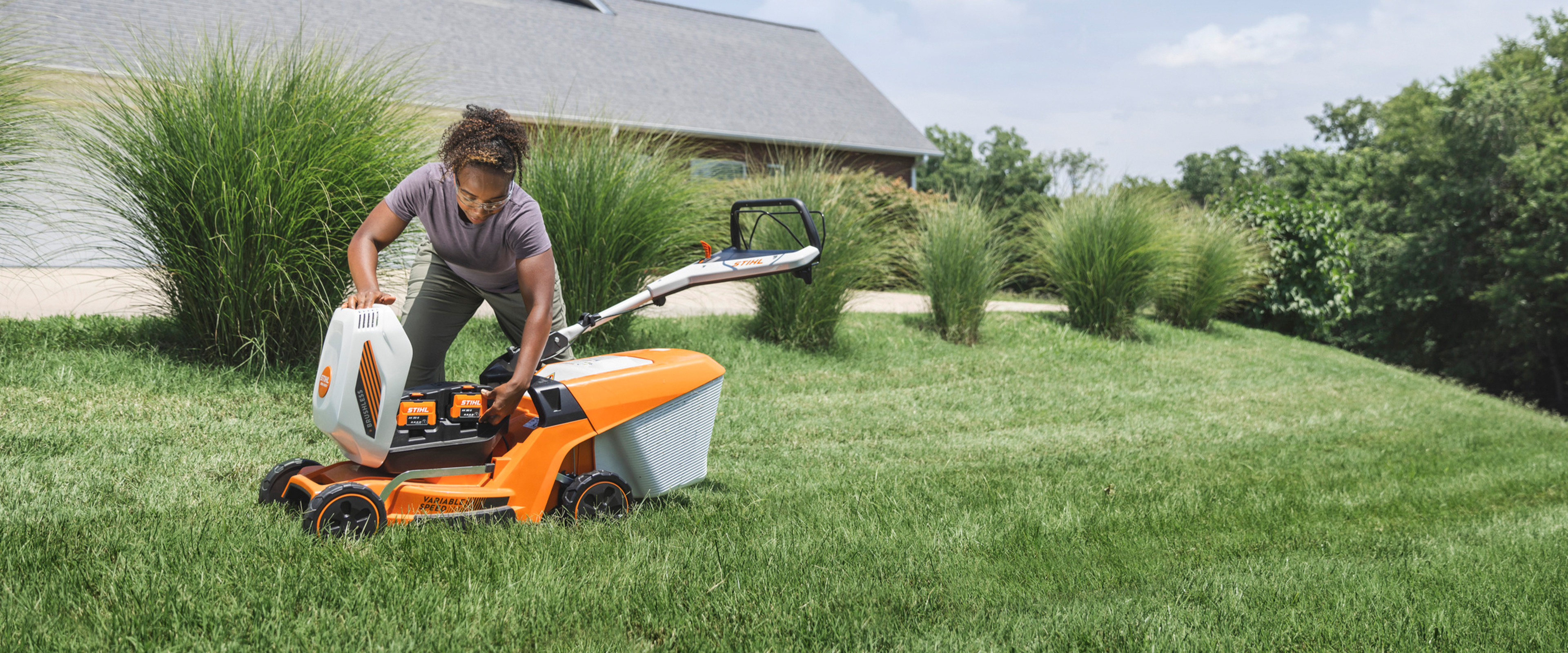 Homeowner loading a battery into a STIHL RMA 3 Series battery-powered push mower on a residential lawn.