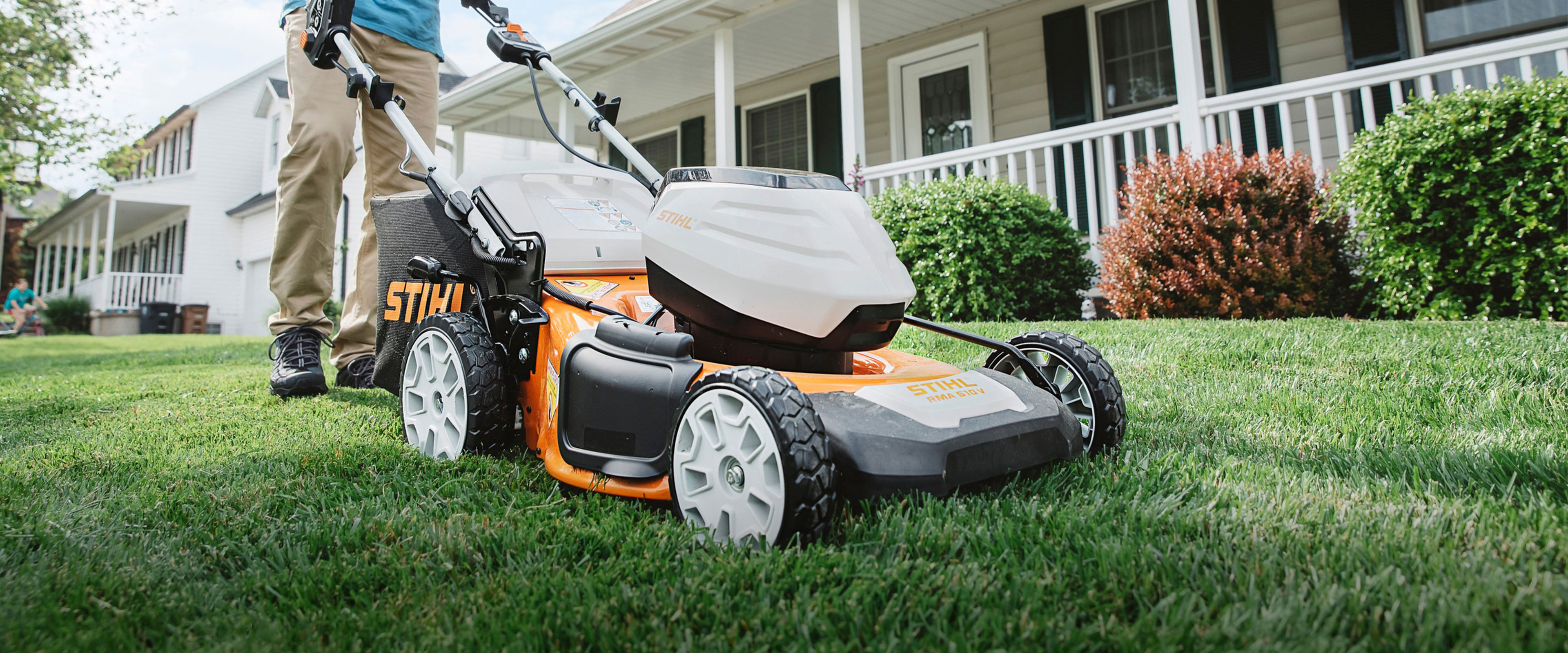 STIHL walk behind lawn mower on a grassy lawn with a person standing behind it near a residential house.