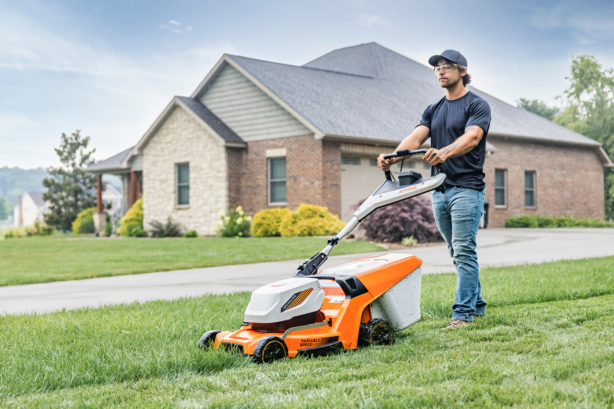 Zoomed out view of a man cutting grass with a STIHL push-mower.