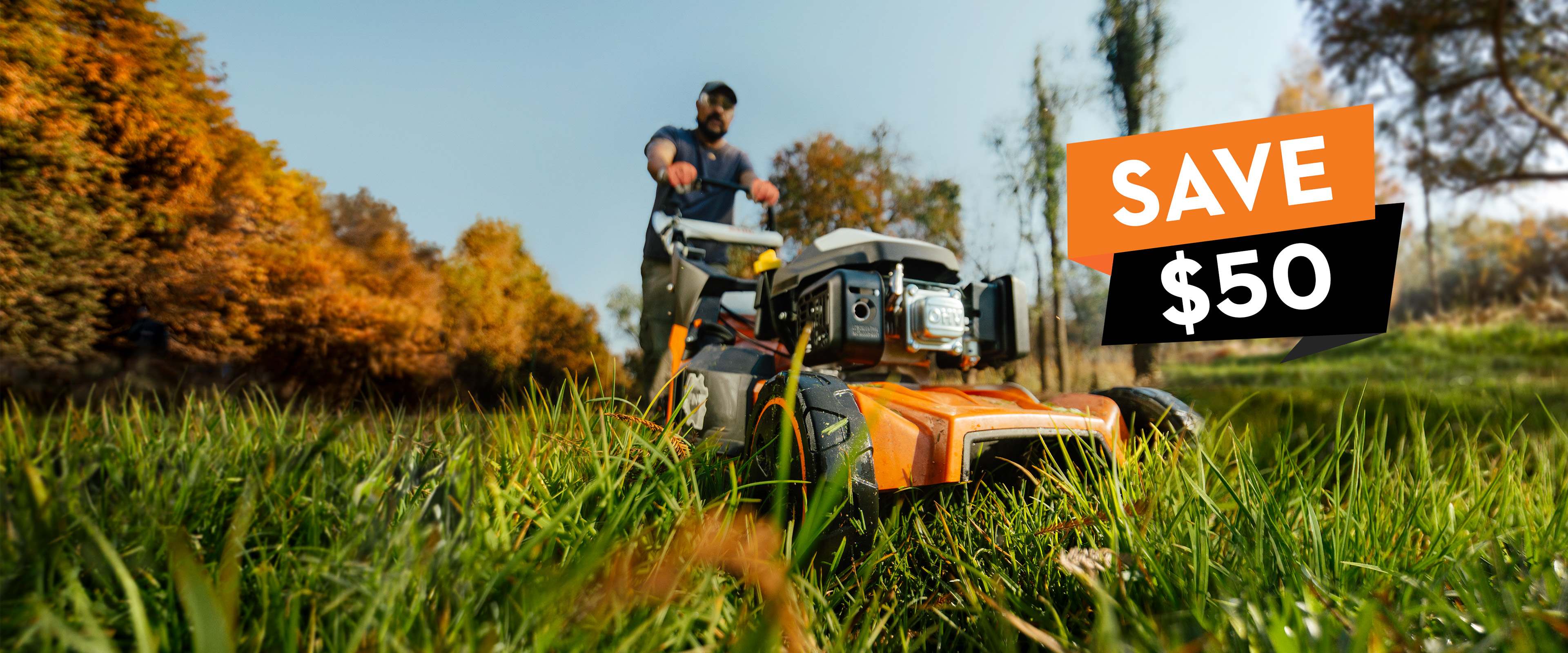 Low close-up angle of a person operating a STIHL RM 453 lawn mower in tall grass with a Save $50 promotional graphic