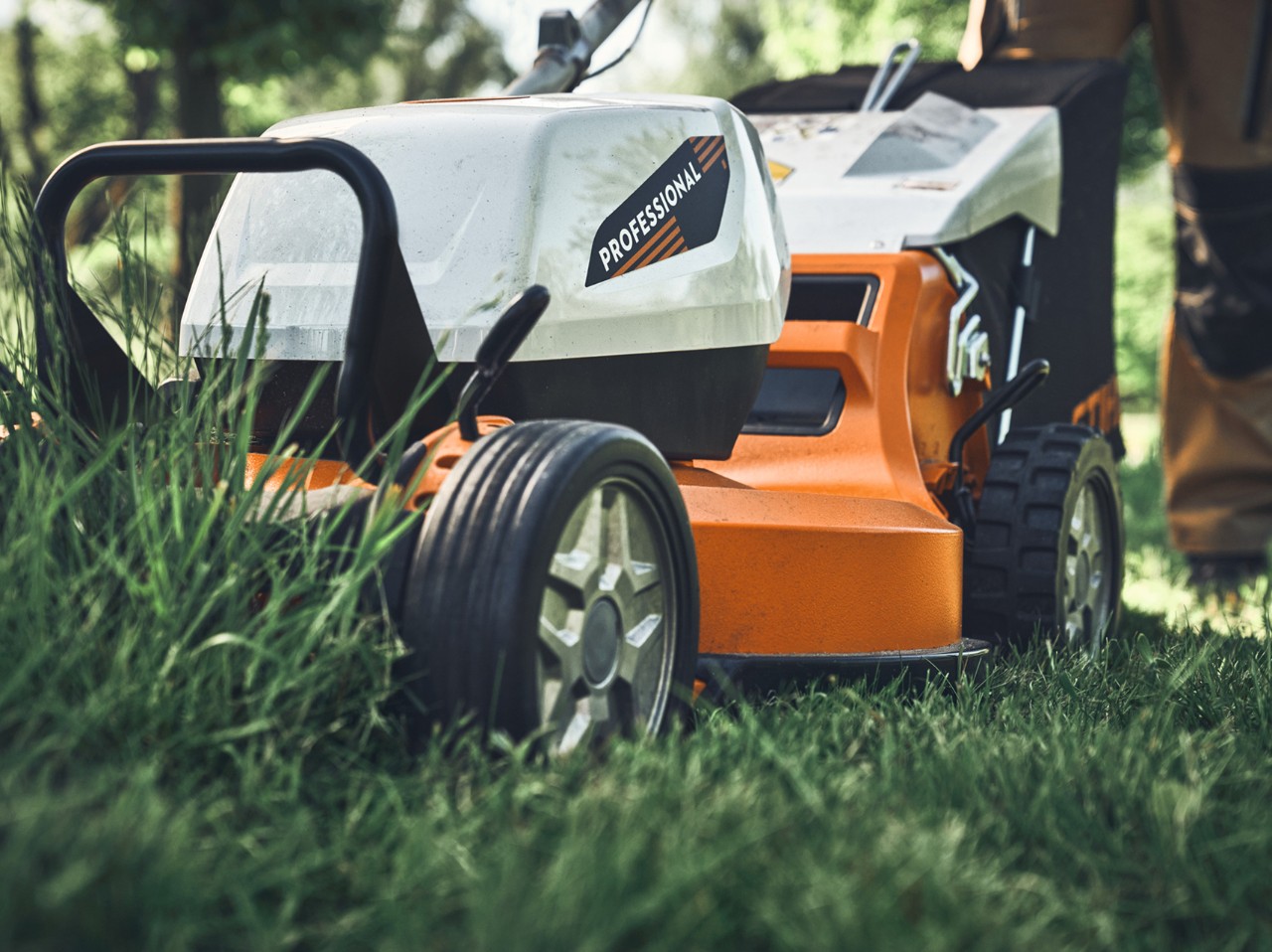A STIHL professional‑grade lawn mower cutting tall grass in an outdoor setting, shown close up from the front with visible wheels and deck.