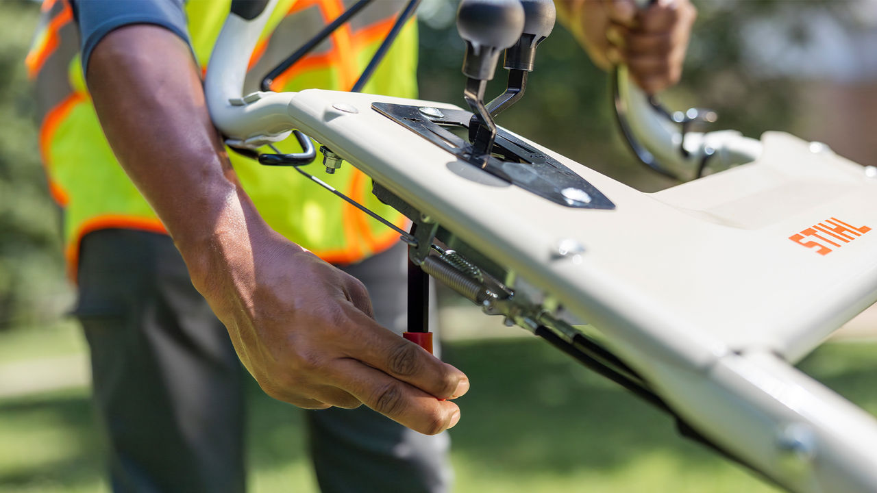 Hand operating the blade brake clutch lever on a STIHL gas mower handlebar.