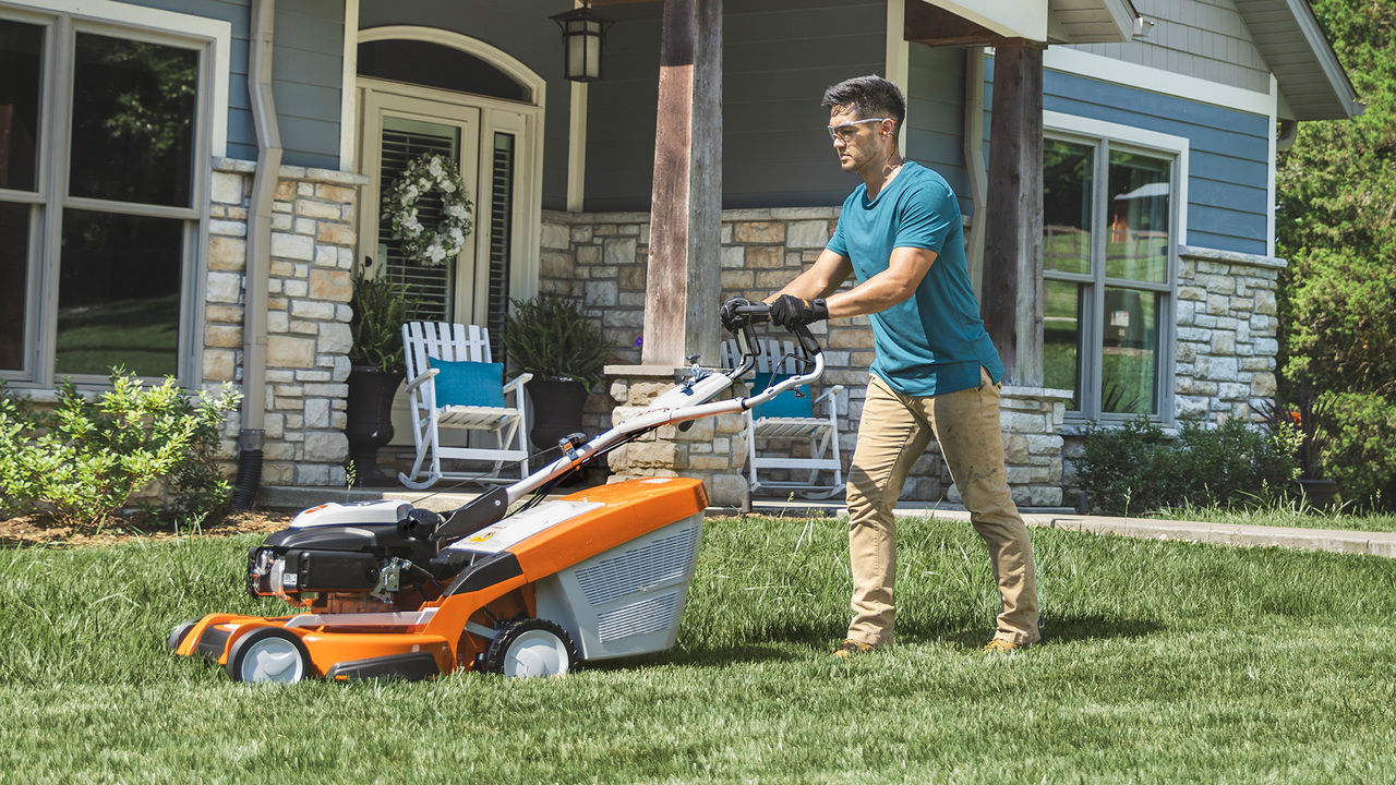 Homeowner mowing a front yard with a STIHL self-propelled gas mower.