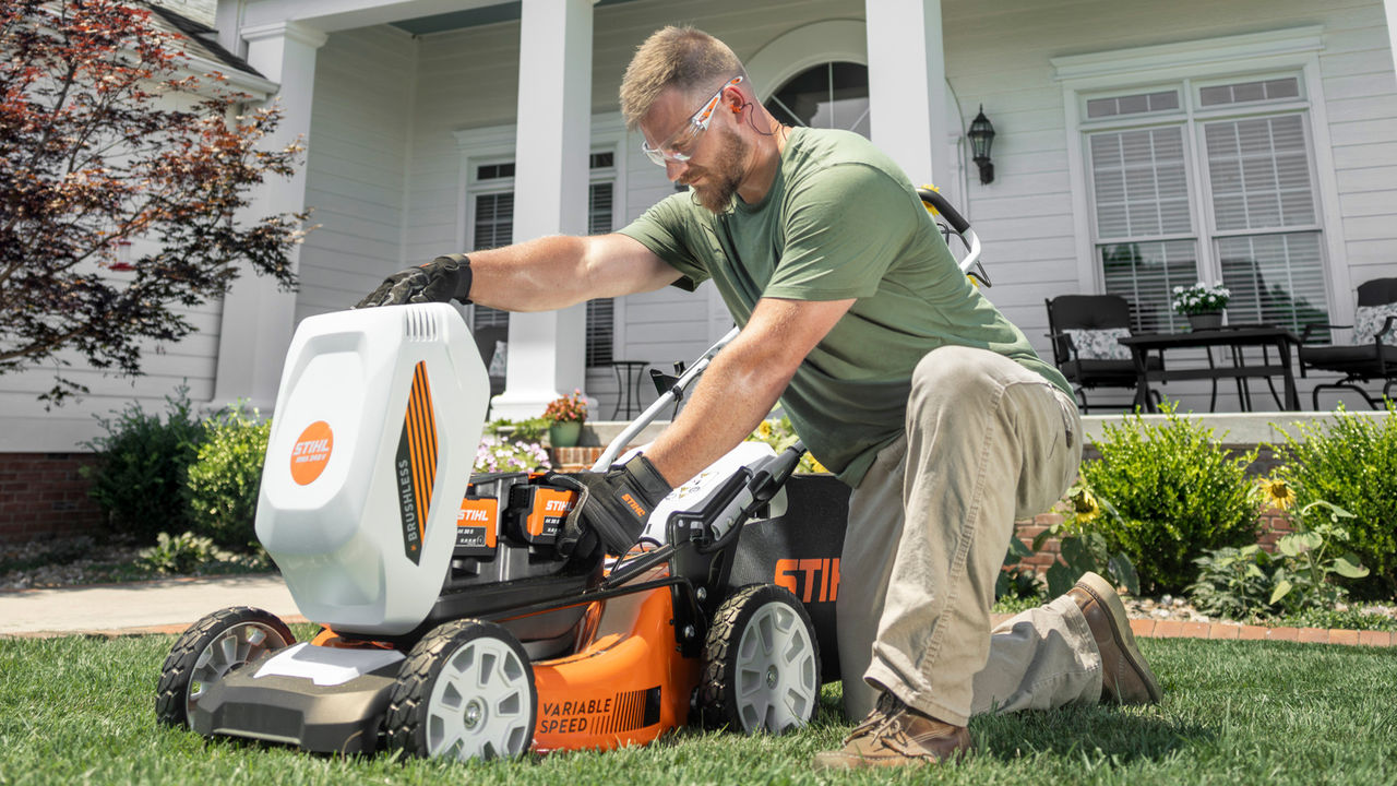 Homeowner installing a battery in a STIHL battery-powered mower in front of a house.