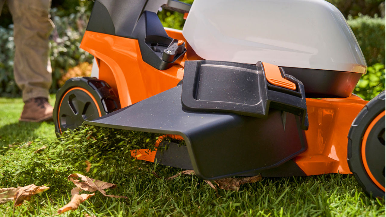 Close-up of a STIHL battery-powered mower deck cutting grass and fallen leaves.