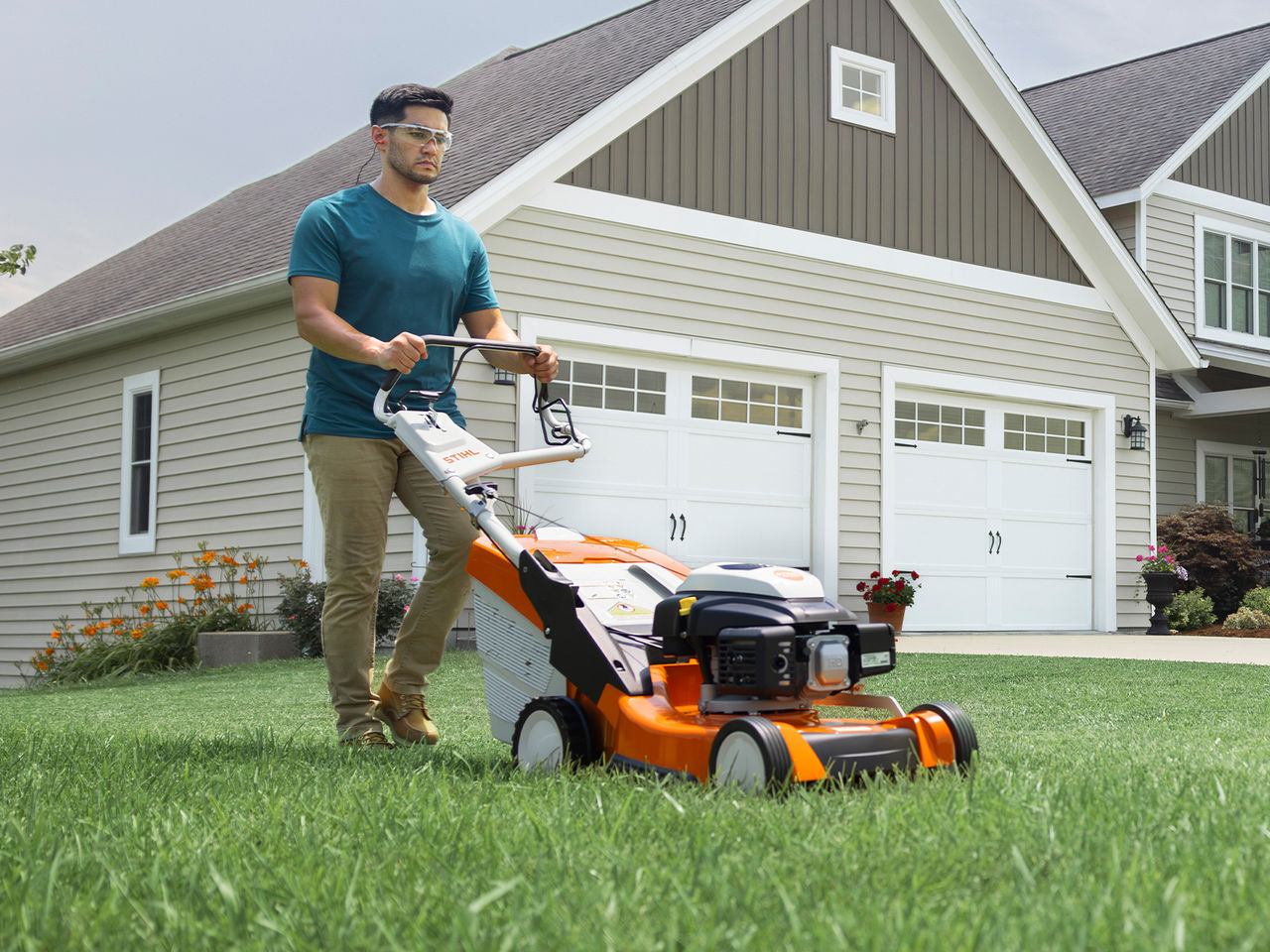 Homeowner mowing past a garage with a STIHL gas-powered push mower.