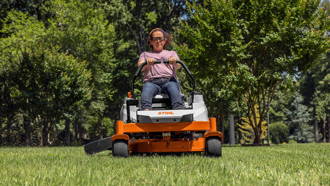 Homeowner riding a STIHL RZ 142 zero-turn mower on a tree-lined lawn.
