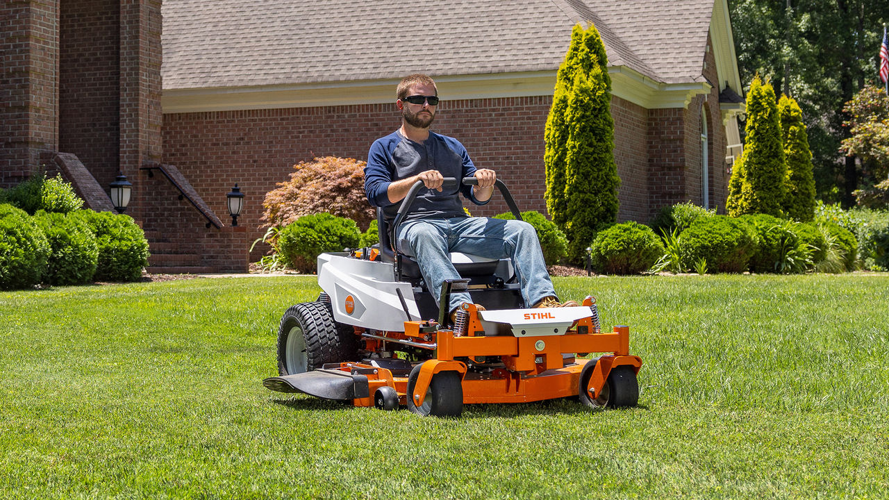 Homeowner riding a STIHL RZ 152 zero-turn mower past a brick home.