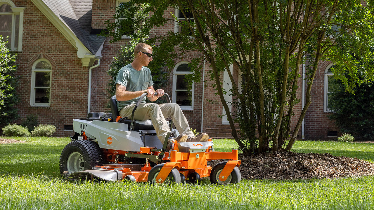 Homeowner riding a STIHL RZ 261 zero-turn mower beside a landscaped garden bed.