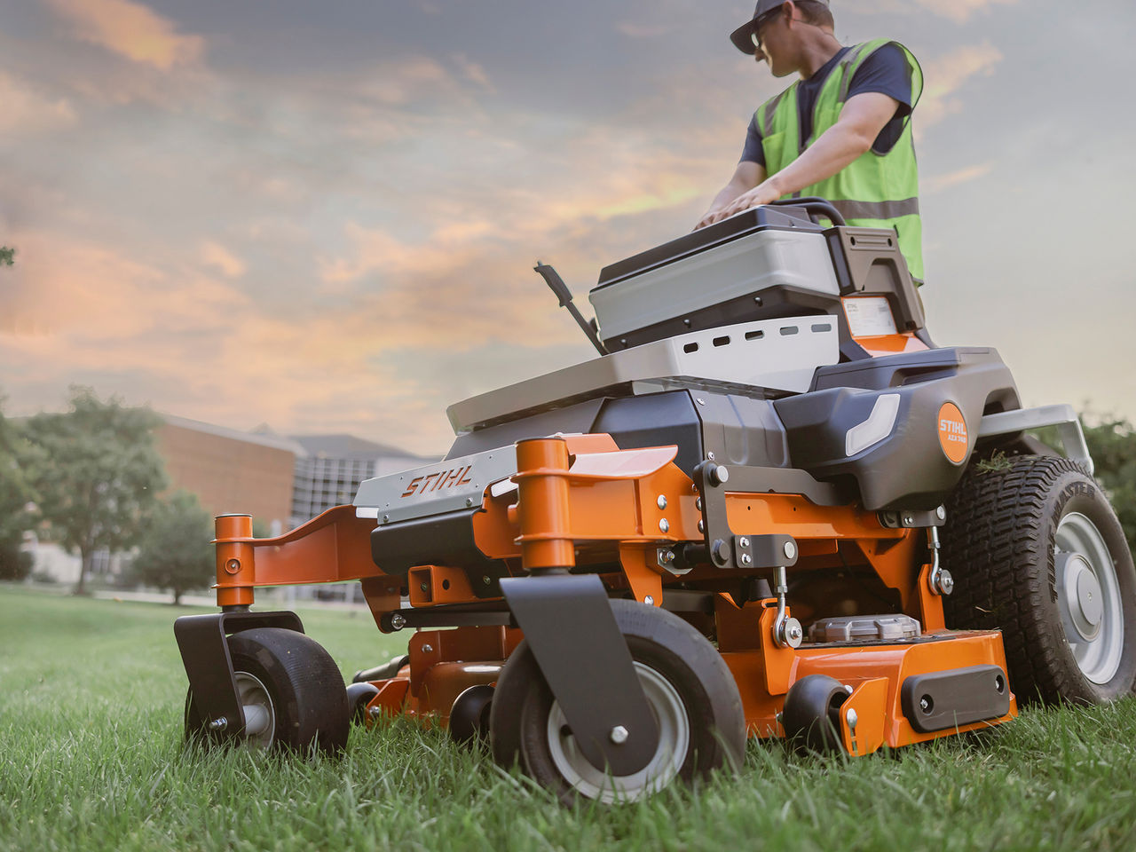 Landscape professional in a safety vest working on a STIHL professional zero-turn mower at sunset.