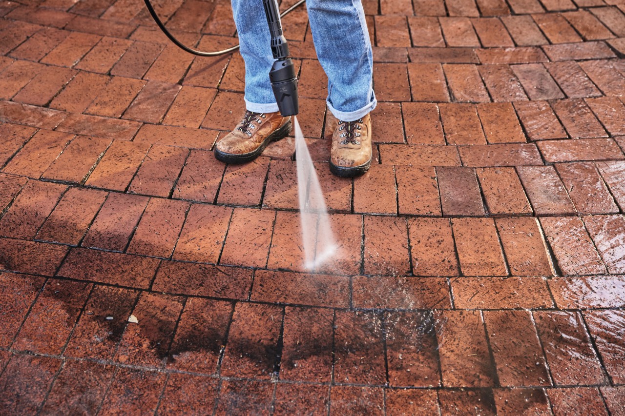 Pressure washer nozzle spraying water to clean a brick patio
