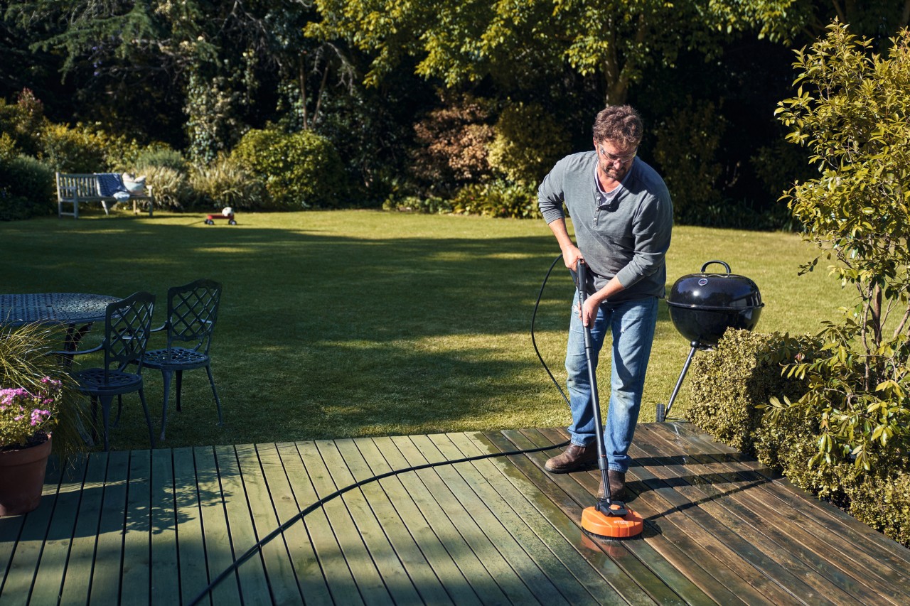 Man using STIHL pressure washer to clean a deck with the surface cleaner attachment a