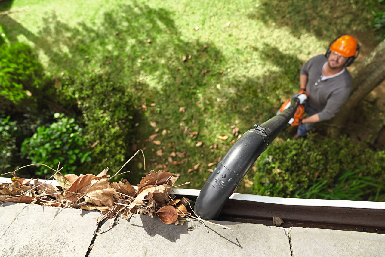 Man using STIHL blower and gutter attachment to remove leaves from gutters.